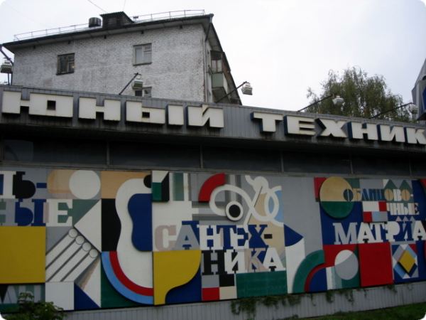 Фасад здания с надписью «ЮНЫЙ ТЕХНИК» и абстрактной мозаикой из геометрических фигур и слов «САНТЕХНИКА», «МАТРИЦА», «ОБЩЕСТВЕННОЕ