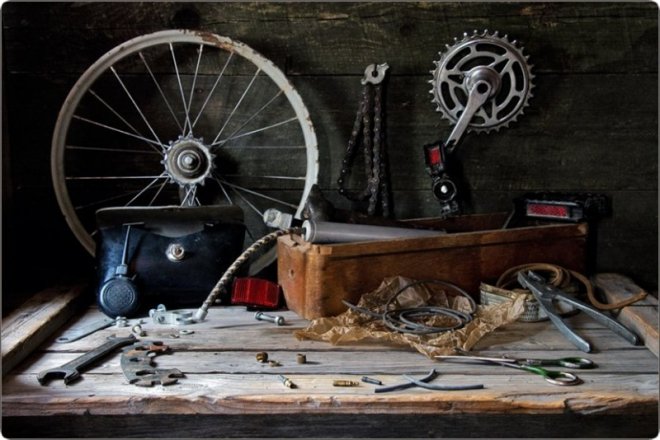 Старые велосипедные детали: колесо, цепь, шестерня, инструменты и сумка на деревянном столе.