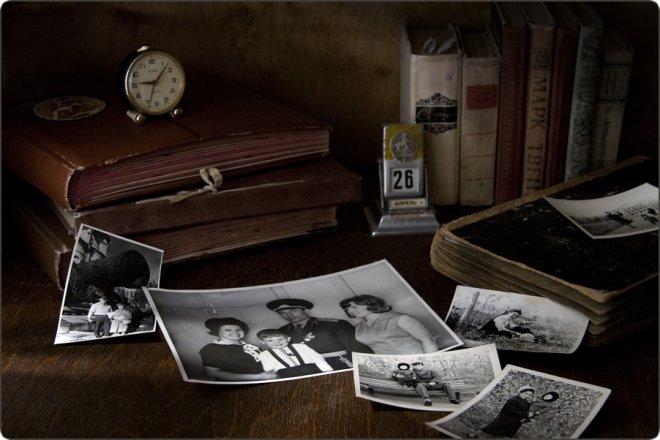 Натюрморт с семейными фотографиями, старыми книгами, будильником и календарём на 26 апреля на деревянном столе.
