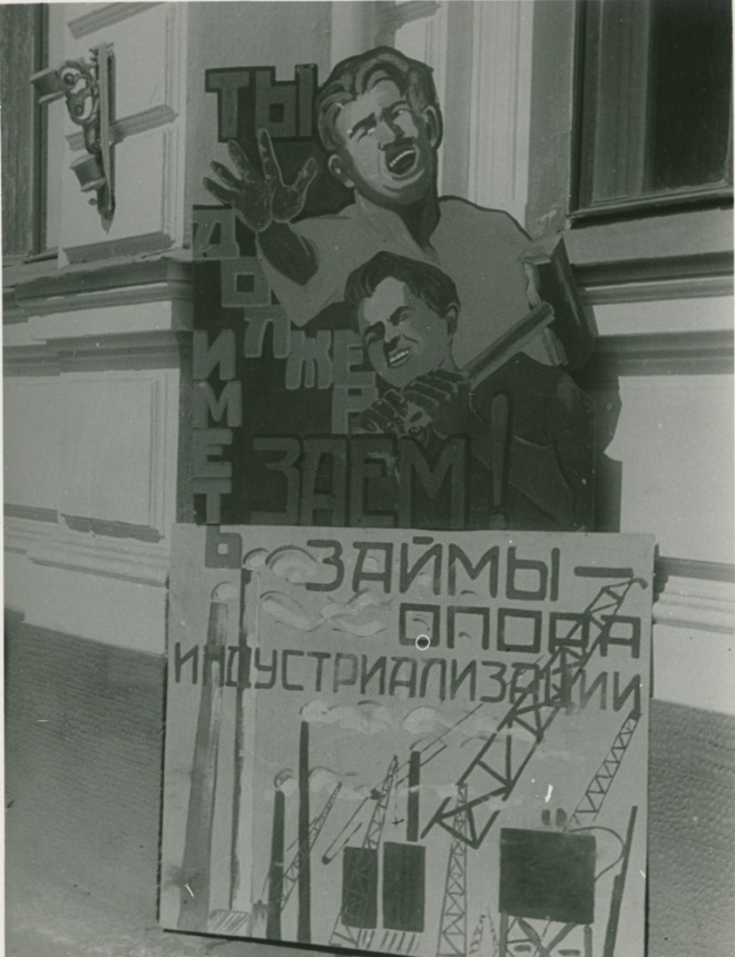 Плакат с надписью «ЗАЙМЫ — ОПОРЫ ИНДУСТРИАЛИЗАЦИИ» и изображением заводов, кранов и рабочих; на заднем плане — другой плакат с кричащим человеком и текстом «ТЫ ДОЛЖЕН ИМЕЕМ ЗАЕМ!