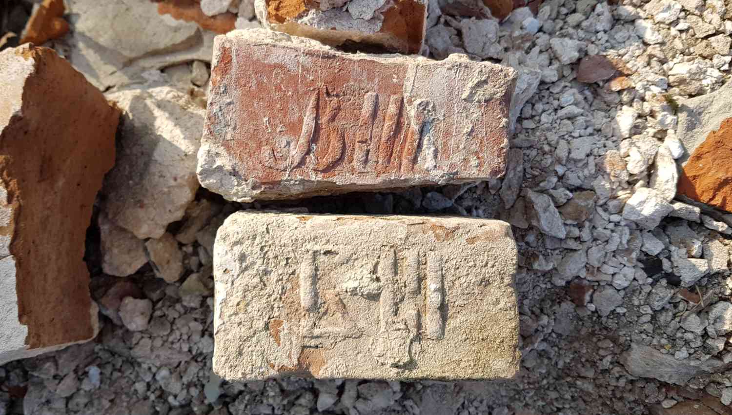 Два кирпича с оттисками клейм «511» и «511» лежат среди обломков бетона и щебня на строительной площадке.