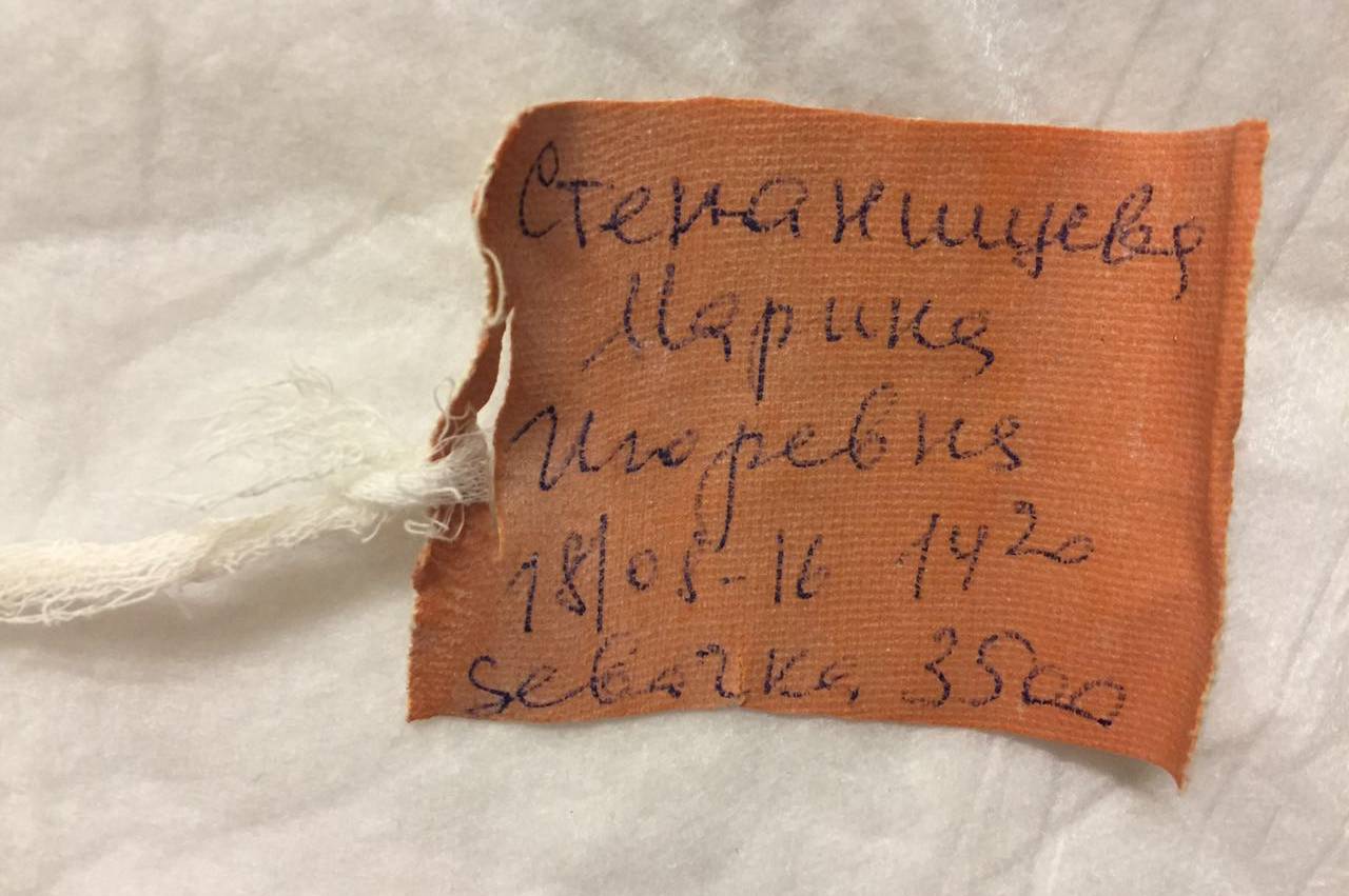 Оранжевая тканевая бирка с рукописной надписью: «Степанищев Маринка Игорева 18/05-16 1420 Севачка, 3500» на белом фоне.