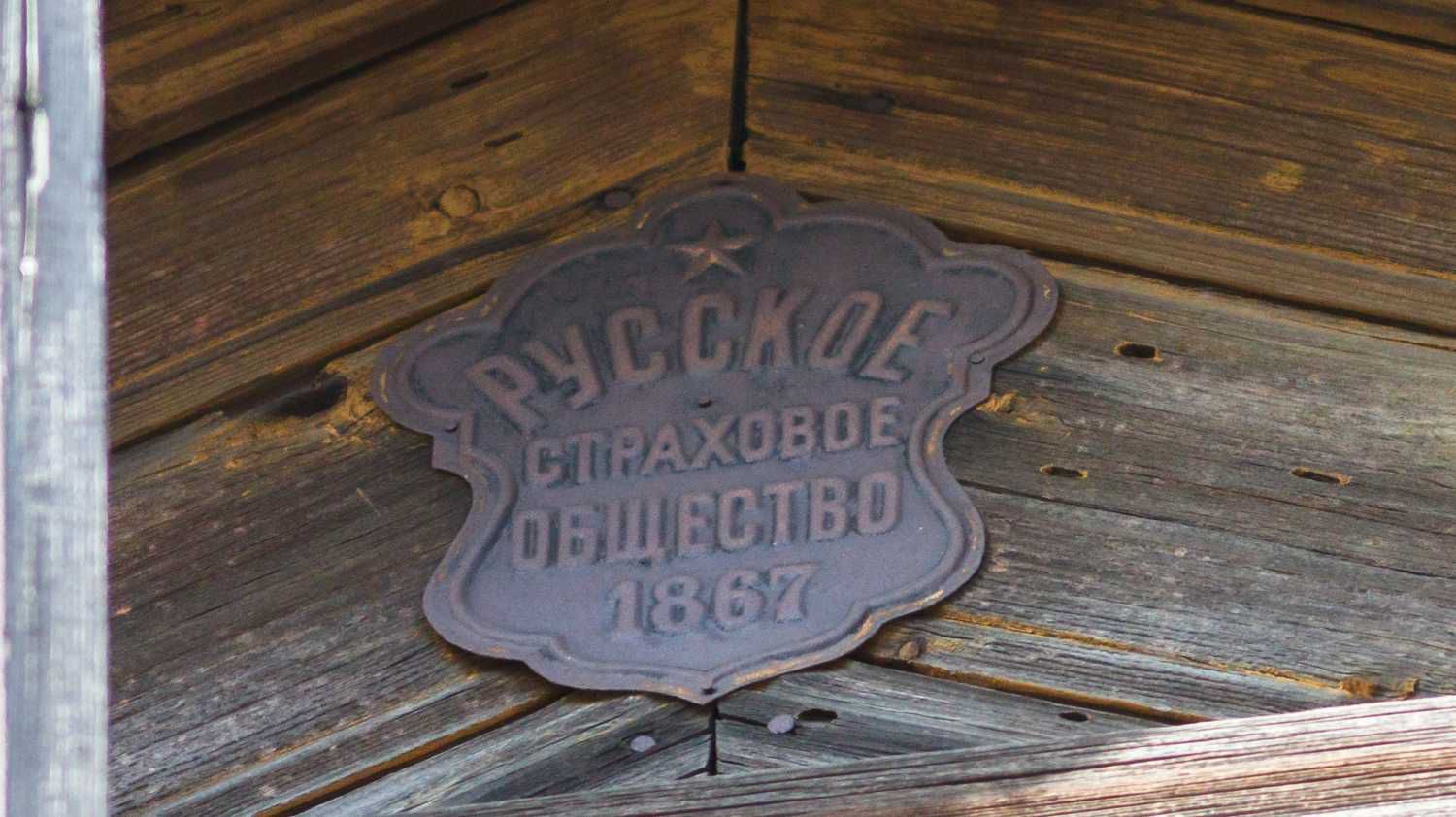 Металлическая табличка с надписью «РУССКОЕ СТРАХОВОЕ ОБЩЕСТВО 1867» и звездой, подвешенная на деревянной стене.