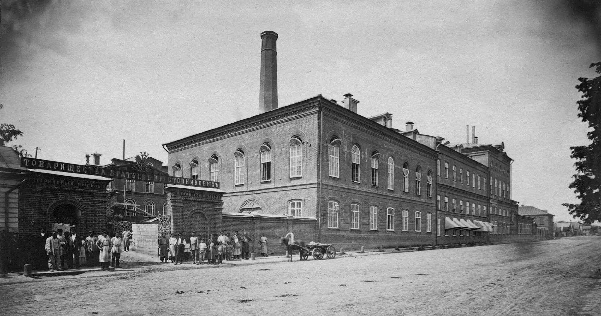 Чёрно-белое фото: заводское здание с высокой трубой, группой рабочих у ворот и конной повозкой; на арке — надпись «ТОВАРИЩЕСТВА БРАТЬЕВ КУСТОВНИКОВЫХЪ».