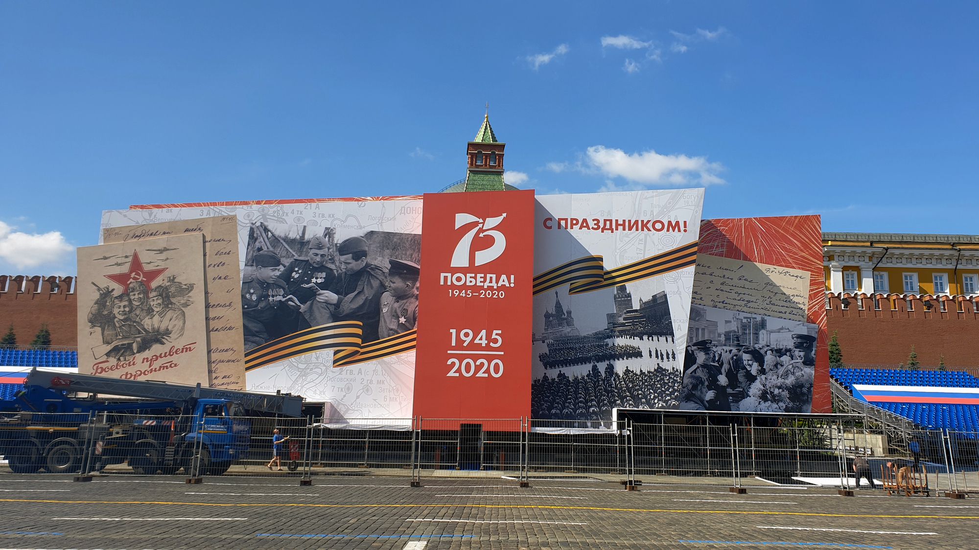 Большой баннер на Красной площади с надписью «ПОБЕДА! 1945–2020», «С ПРАЗДНИКОМ!» и историческими фотографиями; видна башня Кремля и триколор.