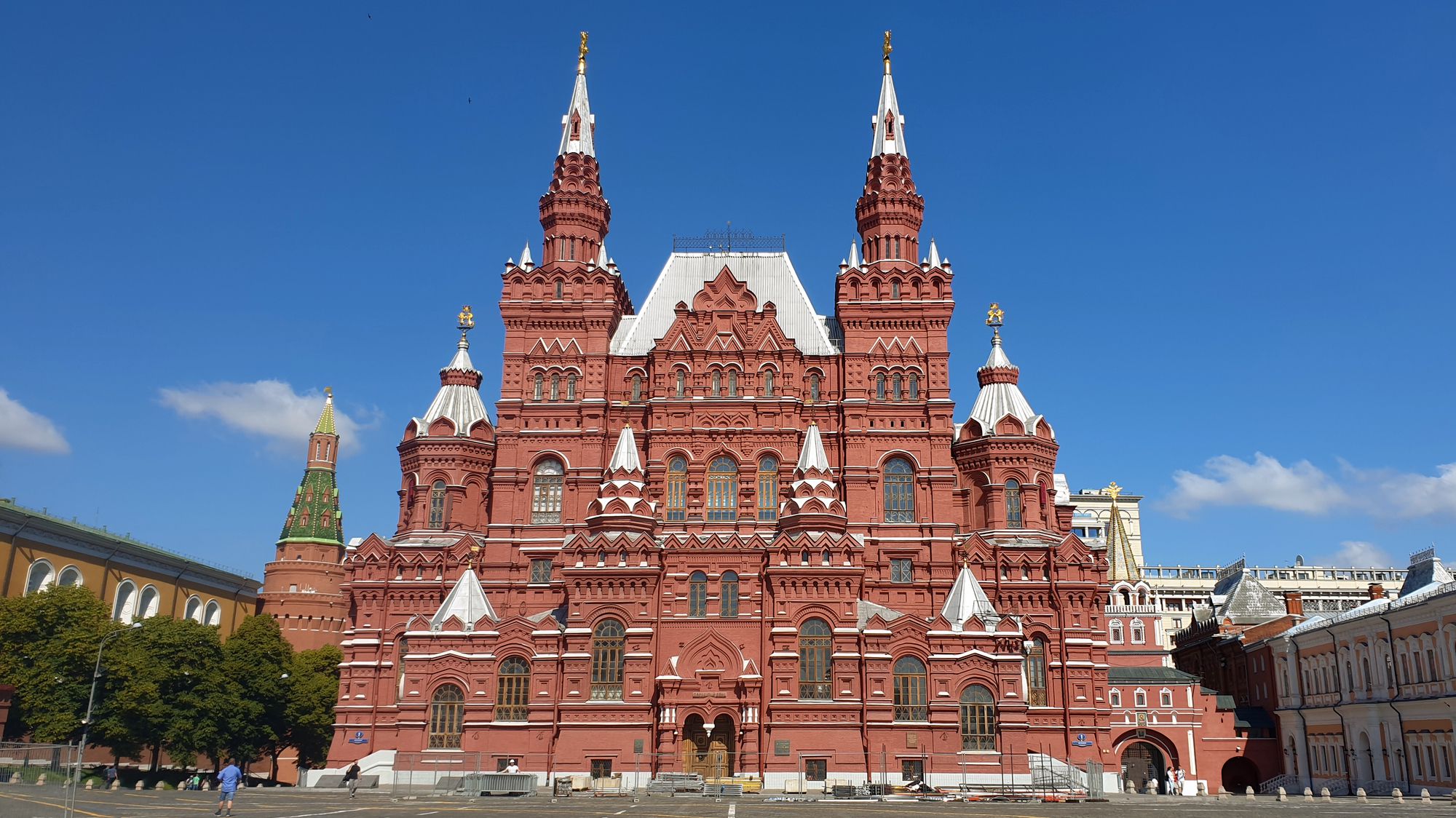 Краснокирпичное здание Государственного исторического музея на Красной площади с высокими башнями и шатрами под ясным голубым небом.