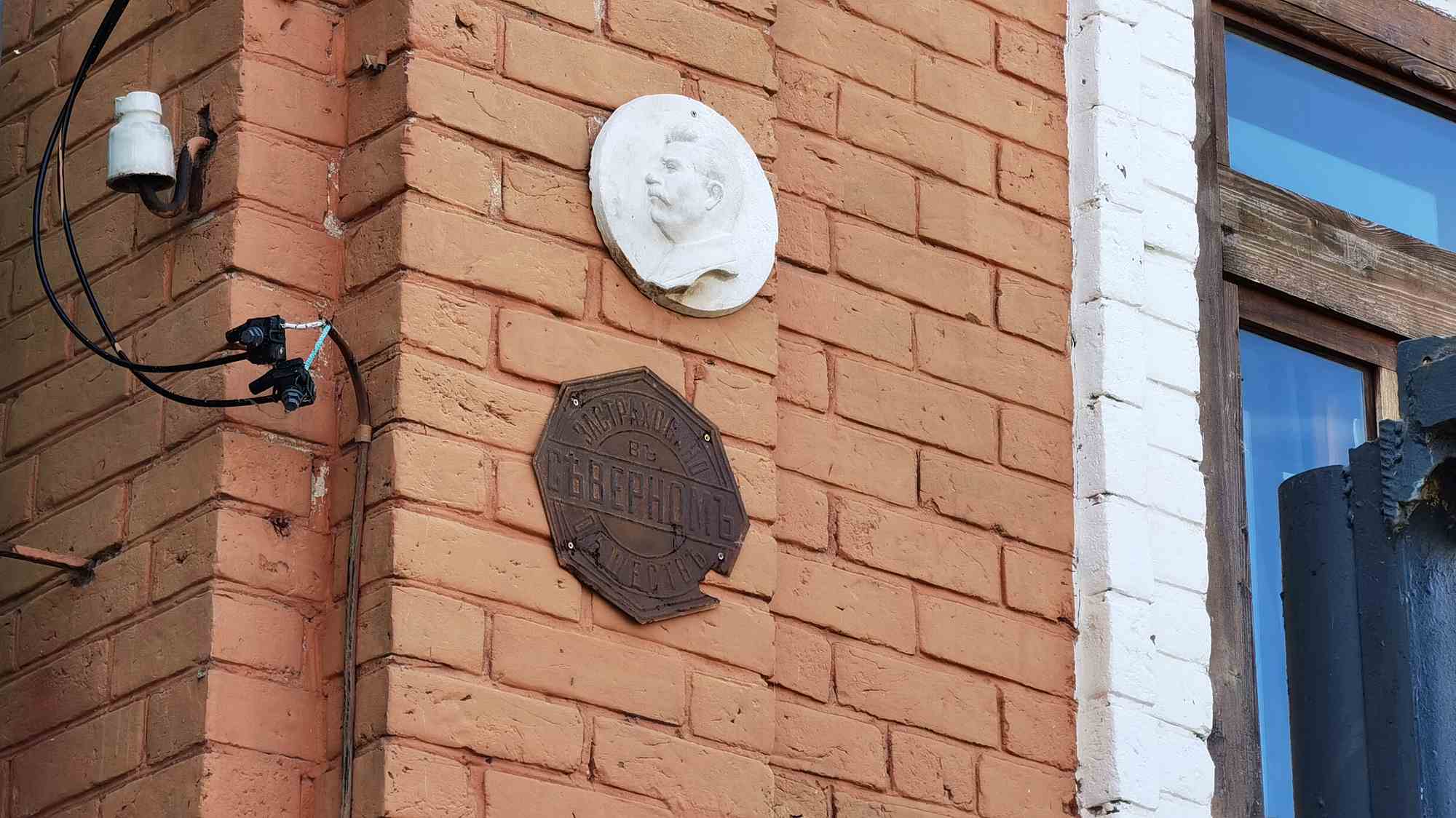 На кирпичной стене здания — белый барельеф Ленина и старинная табличка «ПОСТРАХОВАНЪ ВЪ СЪВЕРНОМЪ» с надписью «МЕСТНО».