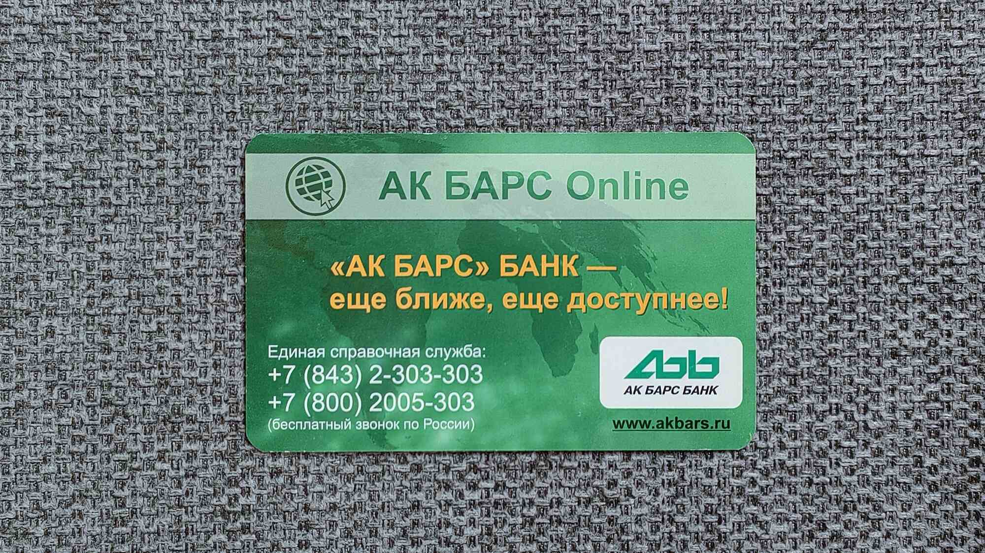 Зелёная визитка АК БАРС Online с логотипом, слоганом «еще ближе, еще доступнее!», номерами справочной службы и сайтом www.akbars.ru на серой тканевой поверхности.