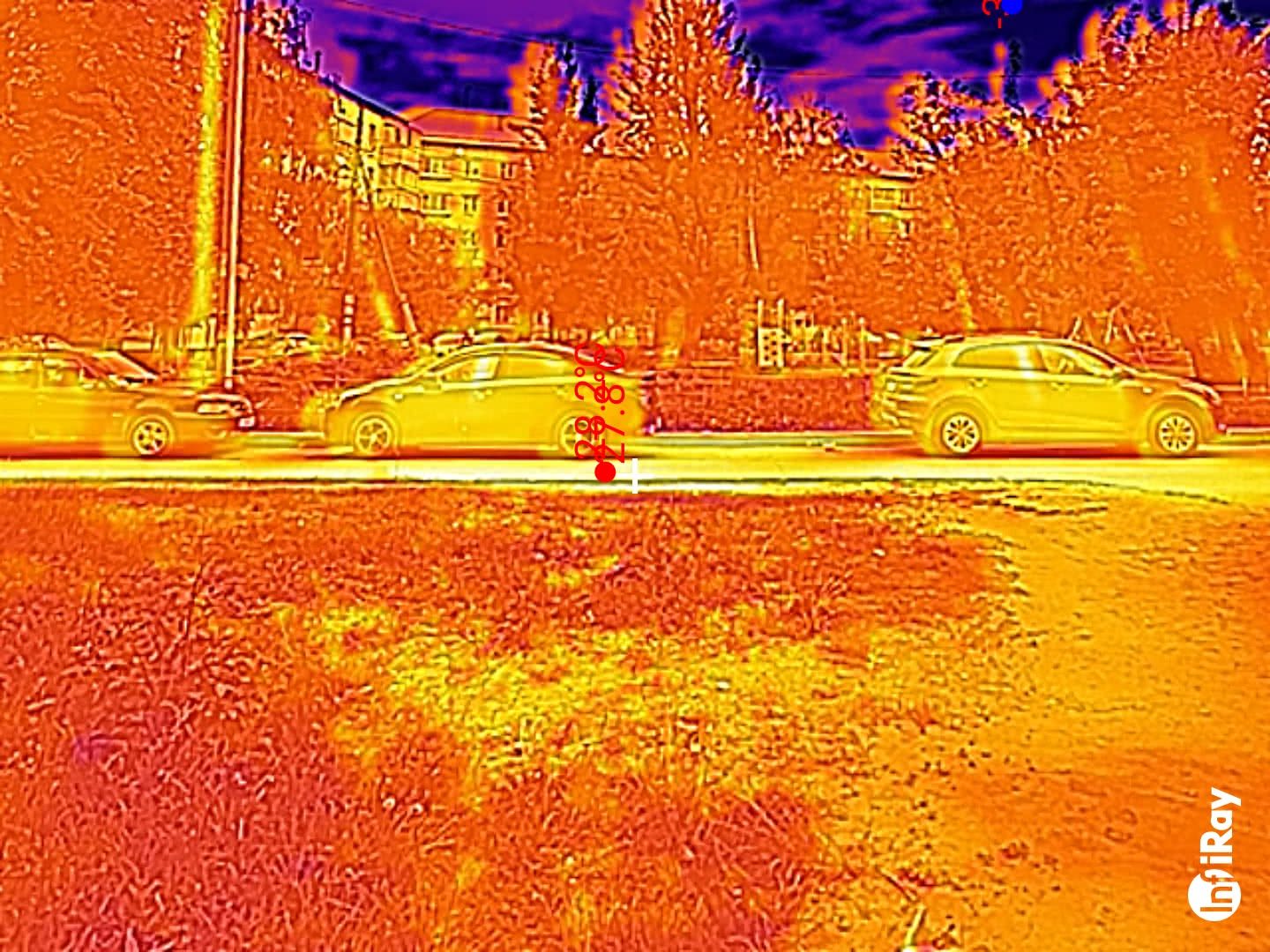 Тепловизионное изображение улицы с тремя автомобилями и зданием на фоне; на центральной машине отображена температура 27,8°C, в правом нижнем углу — логотип FLIR.