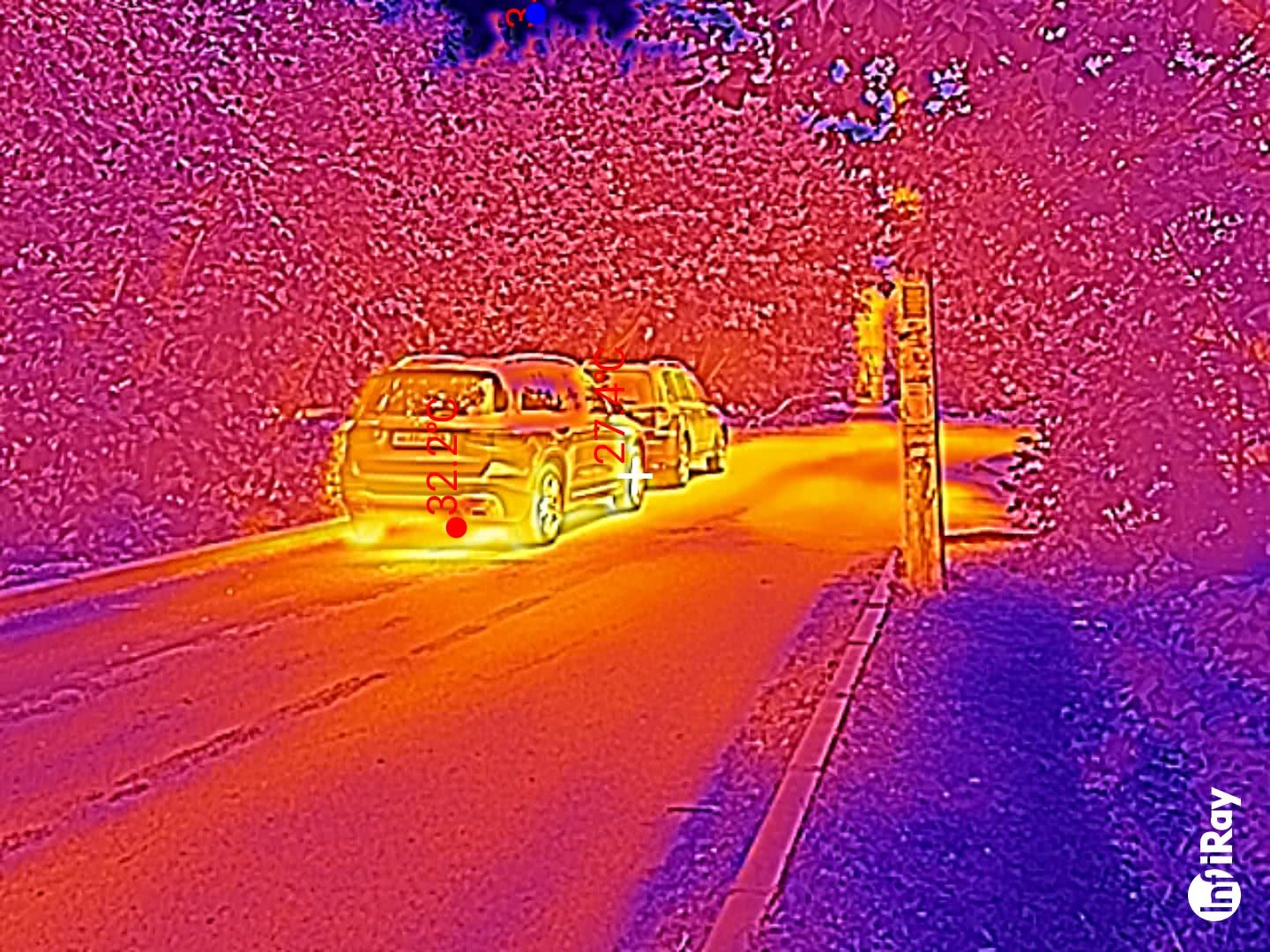 Тепловизионное изображение двух автомобилей на дороге: температура кузова первого — 32,2°C, второго — 27,4°C; справа — столб, фон — деревья; логотип InfiRay в углу.