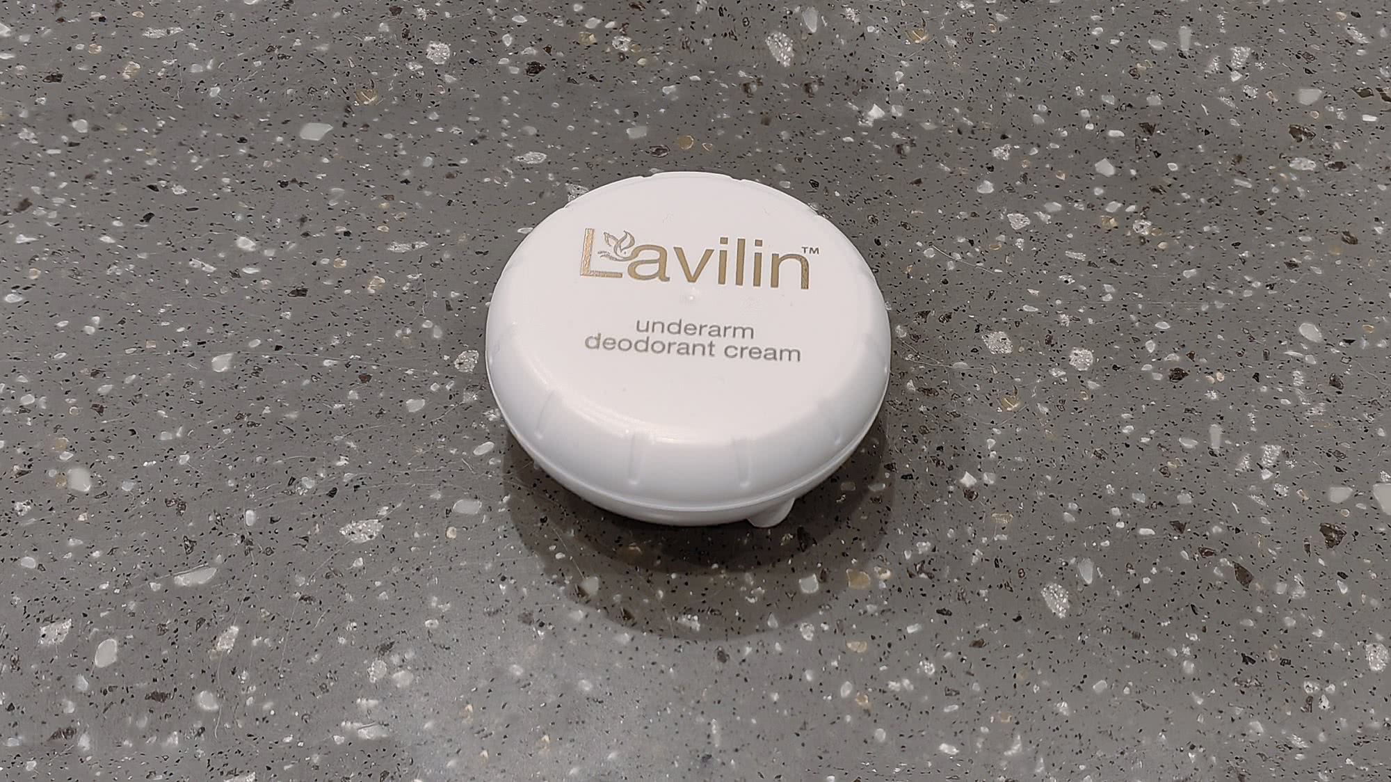 Белая круглая баночка дезодоранта Lavilin для подмышек с золотистым логотипом на сером мраморном фоне.