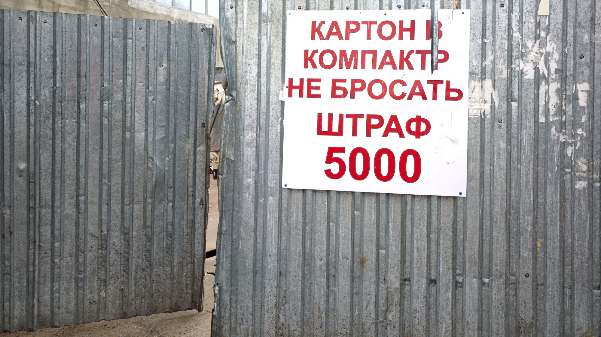 Белый знак с красным текстом на металлической стене: «КАРТОН В КОМПАКТ НЕ БРОСАТЬ ШТРАФ 5000».
