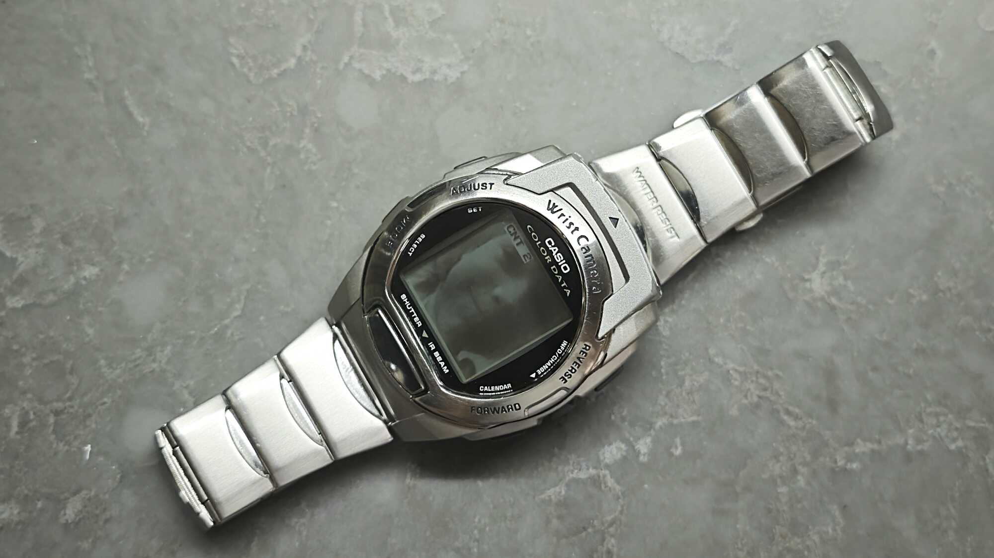 Серебристые наручные часы Casio Wrist Camera с цифровым экраном, надписями «COLOR DATA», «SHUTTER», «IR BEAM» и металлическим браслетом на сером фоне.