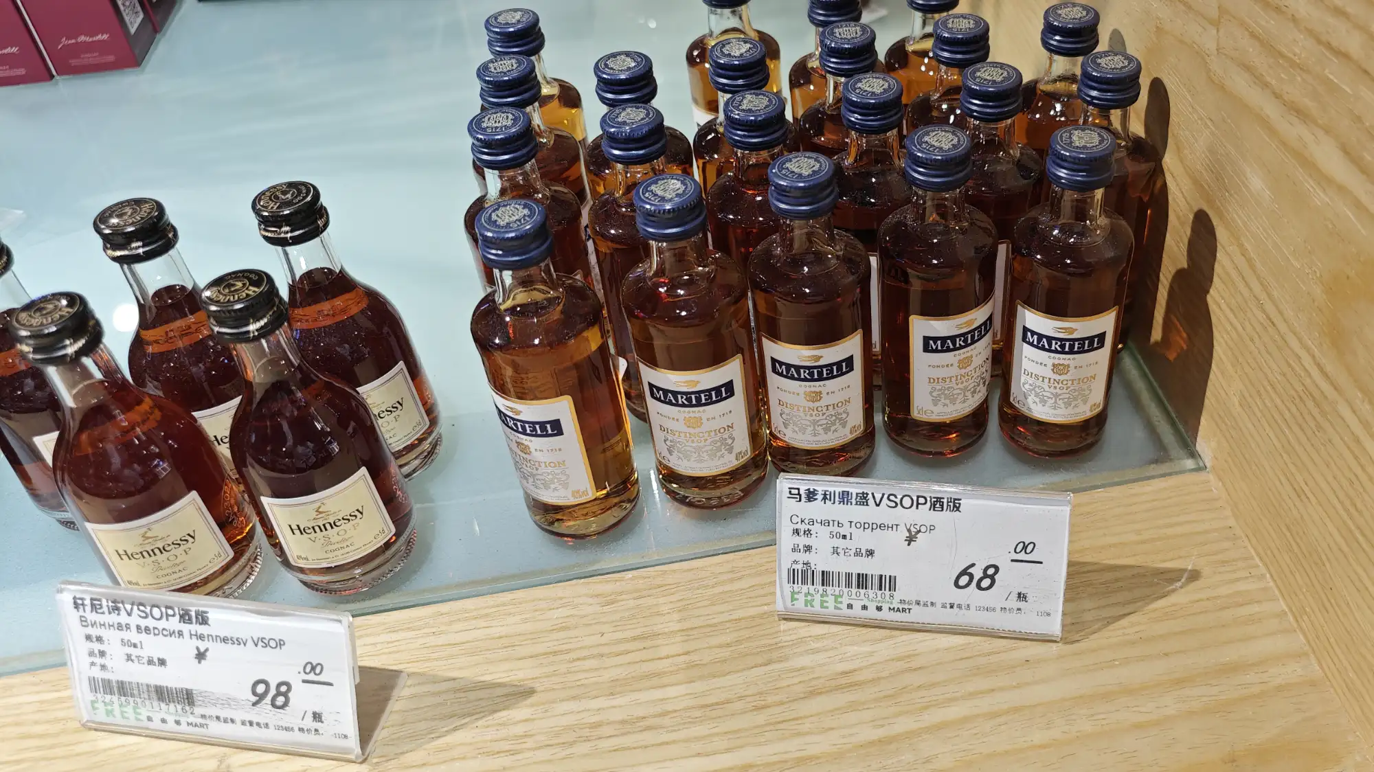 Миниатюрные бутылки Hennessy VSOP и Martell VSOP на стеклянной полке с ценниками: 98 и 68 юаней за 50 мл, надписи на русском и китайском.