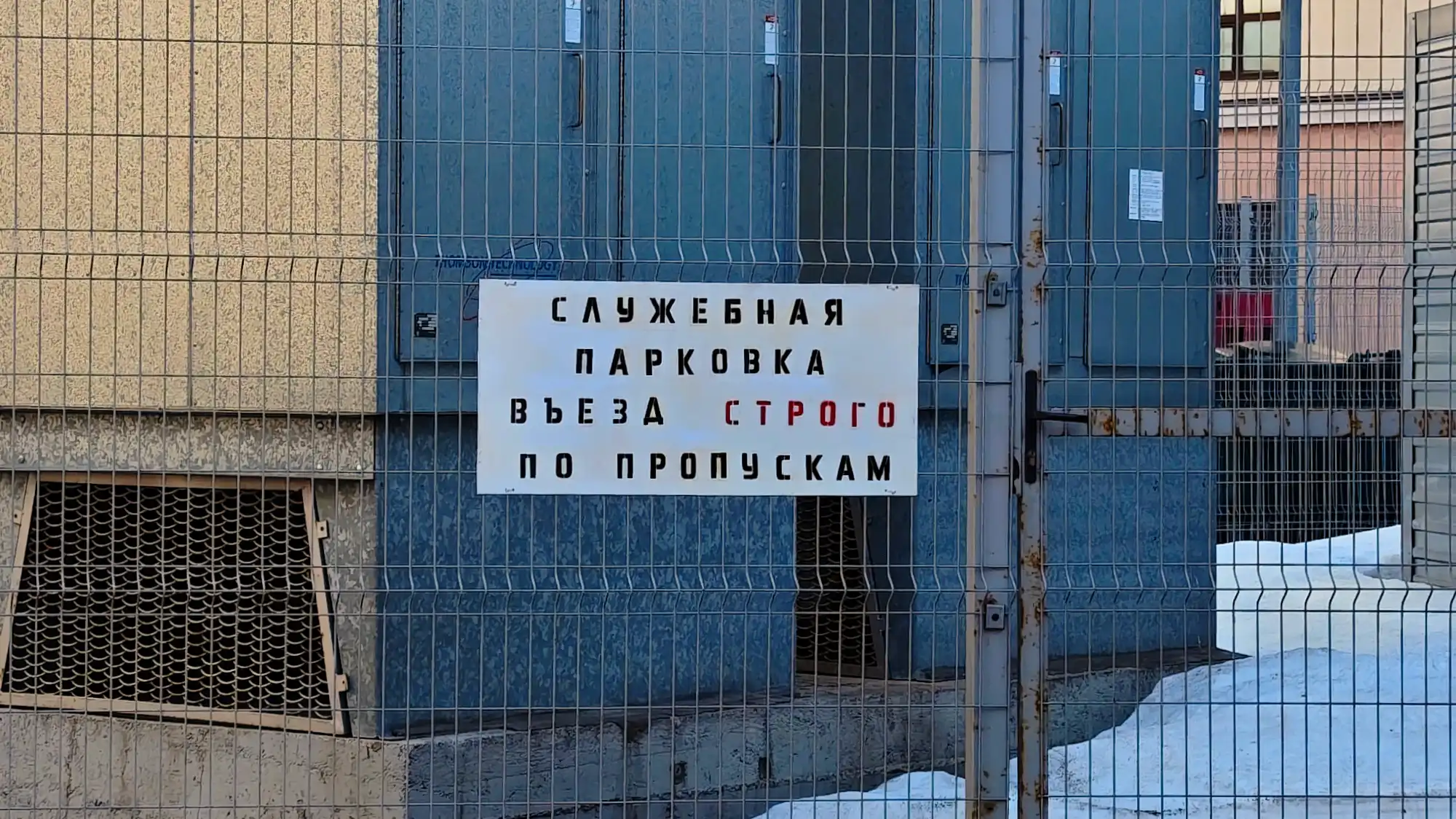 Белый знак на металлической сетке: «СЛУЖЕБНАЯ ПАРКОВКА ВЪЕЗДА СТРОГО ПО ПРОПУСКАМ», слово «СТРОГО» выделено красным.